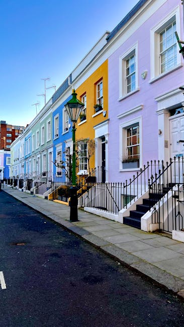 A row of colorful Victorian-style terraced houses on Old Brompton Road near South Kensington, featuring pastel facades in shades of purple, yellow, blue, and white. Each house has a black wrought iron staircase and railing leading up to the front door, with some staircases and railings showing signs of recent cleaning and maintenance. The street is lined with a classic black lamp post, and the pavement appears clean and well-kept. Bright sunlight enhances the vibrant colors of the buildings, highlighting the neatness and upkeep of the residential area. Brompton Carpet Cleaning specializes in surface cleaning, deep cleaning, and sanitisation services to maintain the hygiene and appearance of such domestic settings.