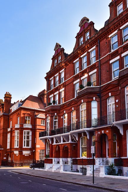 A row of colorful Victorian-style terraced houses on Old Brompton Road near South Kensington, featuring pastel facades in shades of purple, yellow, blue, and white. Each house has a black wrought iron staircase and railing leading up to the front door, with some staircases and railings showing signs of recent cleaning and maintenance. The street is lined with a classic black lamp post, and the pavement appears clean and well-kept. Bright sunlight enhances the vibrant colors of the buildings, highlighting the neatness and upkeep of the residential area. Brompton Carpet Cleaning specializes in surface cleaning, deep cleaning, and sanitisation services to maintain the hygiene and appearance of such domestic settings.